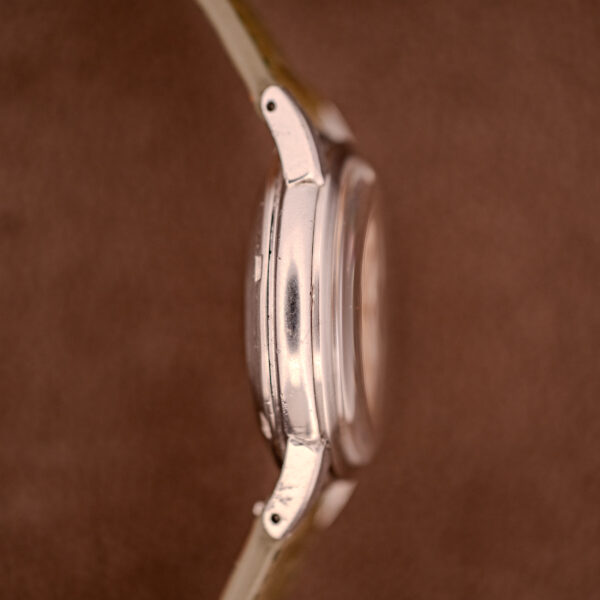 Side view of a silver Omega Transitional Calendar Bumper Automatic Ref. 2438-2 Cal. 353 c.1951 wristwatch case with lugs, featuring the Cal. 353 movement, set against a brown background.