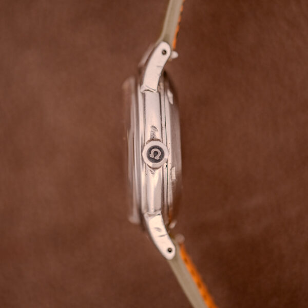 Side view of an Omega Transitional Calendar Bumper Automatic Ref. 2438-2 Cal. 353 c.1951 wristwatch in silver, featuring an Omega logo on the crown, set against a brown background.