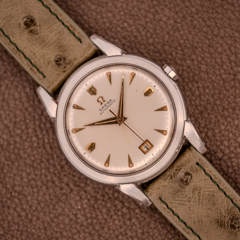 The Omega Transitional Calendar Bumper Automatic Ref. 2438-2 Cal. 353 (c.1951) features a cream dial with date at 3 o’clock, Cal. 353 automatic movement, and a tan leather strap.