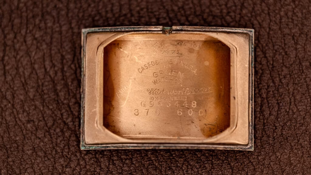 Close-up of the inside case back of a vintage Gruen watch with engraved numbers and text on a leather surface.