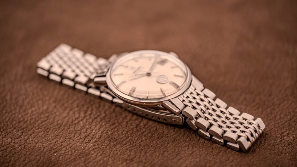 A vintage Omega Seamaster DeVille wristwatch with a silver metal band rests elegantly on a brown textured surface.