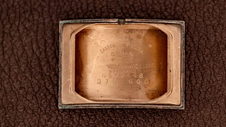 Close-up of the inside case back of a vintage Gruen watch with engraved numbers and text on a leather surface.