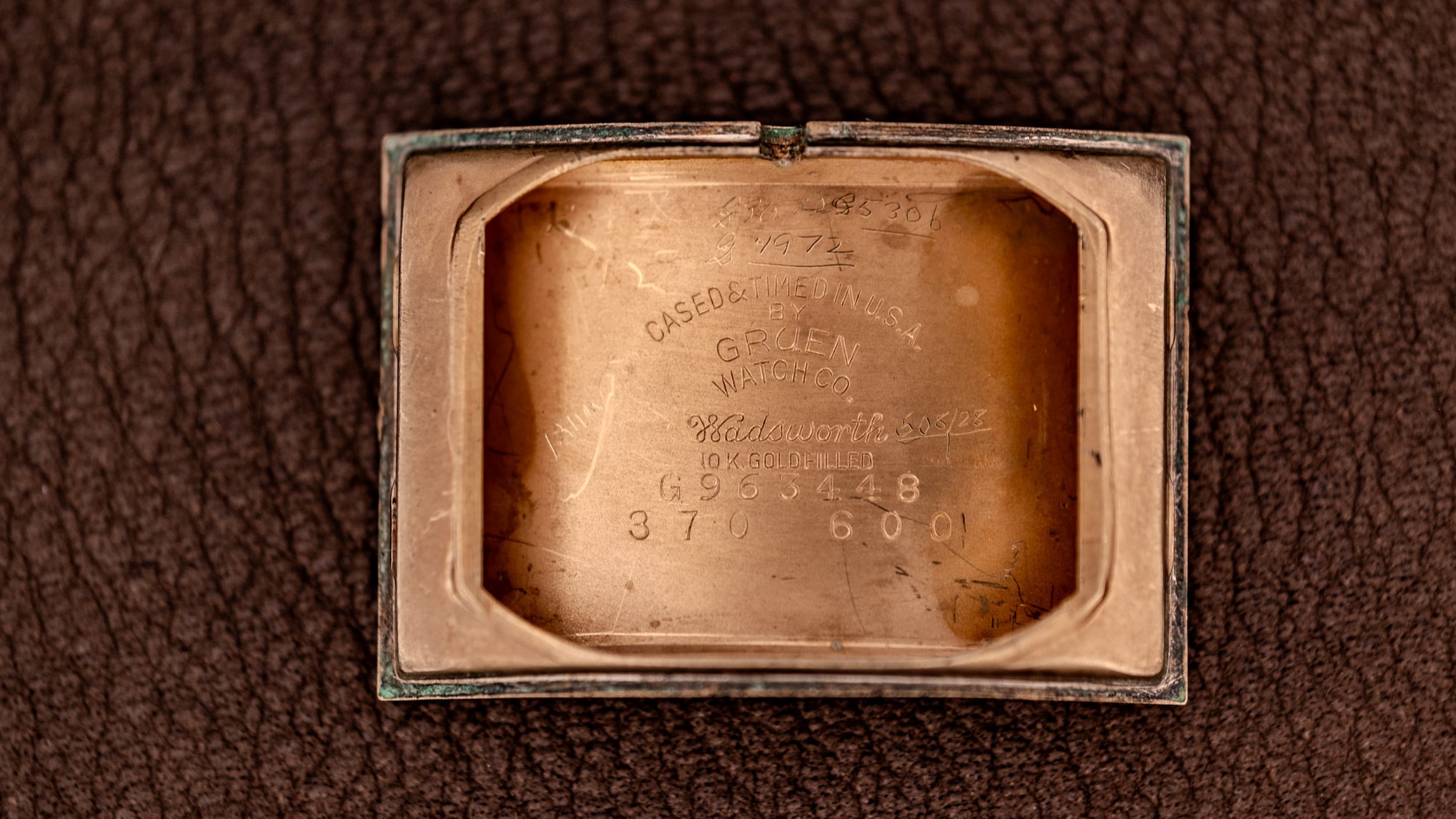 Close-up of the inside case back of a vintage Gruen watch with engraved numbers and text on a leather surface.