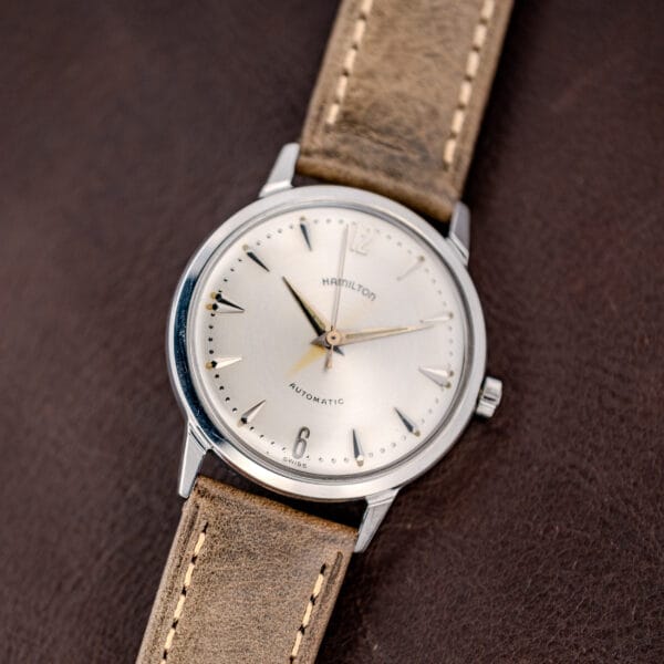 The Hamilton Automatic Silver Sunburst Micro-Rotor Cal. 666 wristwatch features a tan leather strap and striking silver sunburst dial, elegantly displayed on brown leather.