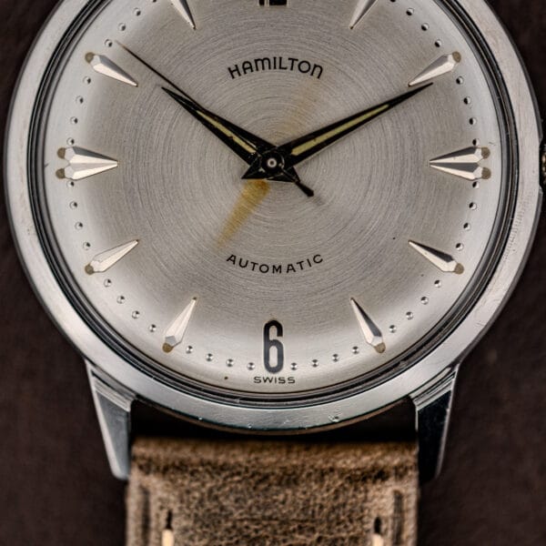 Close-up of the Hamilton Automatic Silver Sunburst Micro-Rotor Cal. 666 wristwatch, showcasing its silver sunburst dial, brown leather strap, and black hour and minute hands.