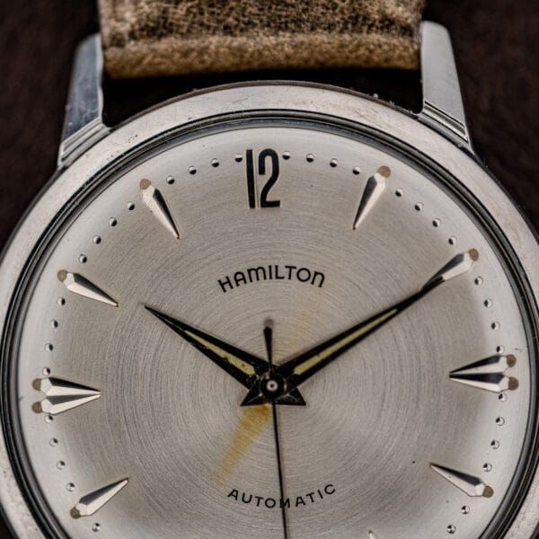 Close-up of a Hamilton Automatic Silver Sunburst Micro-Rotor Cal. 666 wristwatch, featuring a silver sunburst dial, black hands, and a brown leather strap.