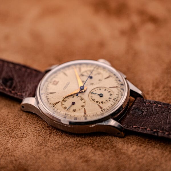 Close-up of a vintage Jaeger Tri-Compax Chronograph Ref. 22522 in stainless steel (Cal. UG 285) with a brown leather strap on a brown suede surface.