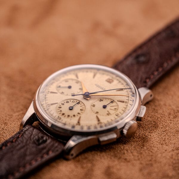 A Jaeger Tri-Compax Chronograph Ref. 22522 in stainless steel with a beige dial and brown leather strap rests on a soft brown surface, showcasing its Cal. UG 285 movement and classic chronograph elegance.