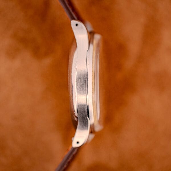 Side view of a Jaeger Tri-Compax Chronograph Ref. 22522 in stainless steel with Cal. UG 285 movement, featuring a brown leather strap, set against a brown background.