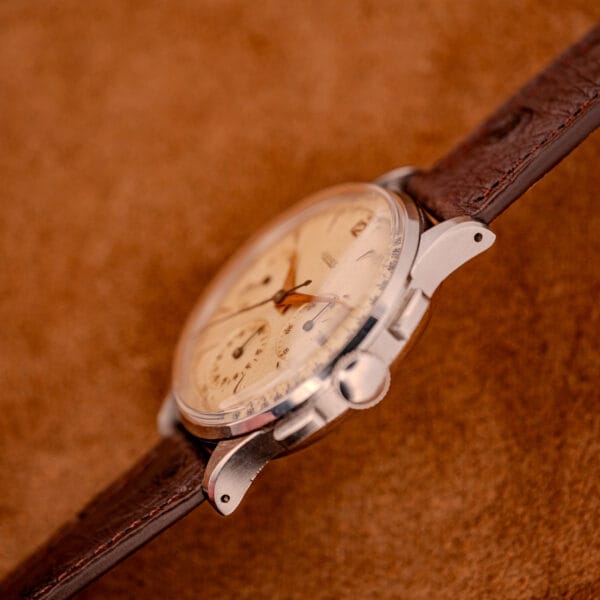 A close-up of a Jaeger Tri-Compax Chronograph Ref. 22522 in stainless steel with Cal. UG 285, featuring a brown leather strap and displayed on a soft brown surface.