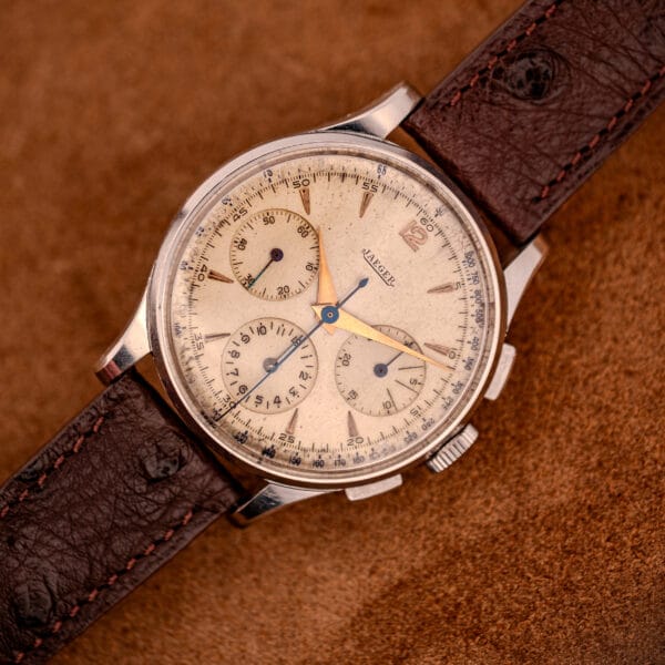 A Jaeger Tri-Compax Chronograph Ref. 22522 in stainless steel with Cal. UG 285, featuring a brown leather strap, beige dial, multiple subdials, blue hands, and classic design.