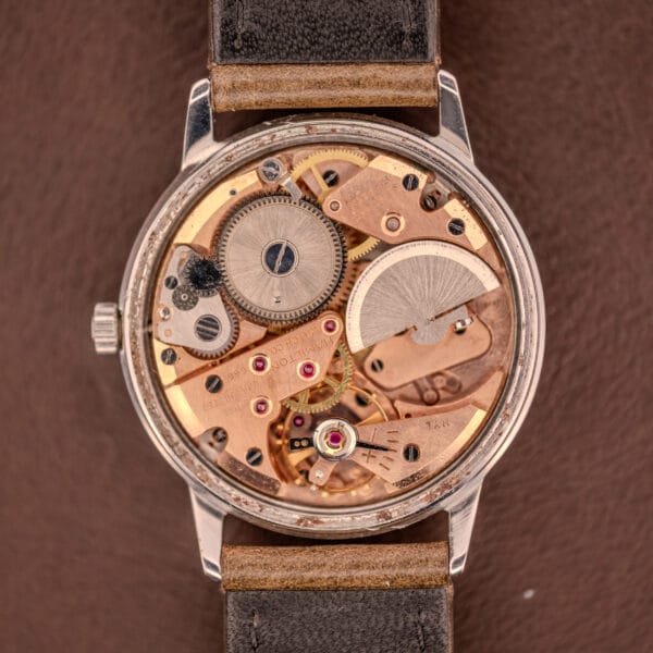 Close-up of an open Hamilton Automatic Silver Sunburst Micro-Rotor Cal. 666, revealing its intricate gears and micro-rotor mechanism against a brown background.