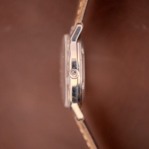 Side view of the Hamilton Automatic Silver Sunburst Micro-Rotor Cal. 666 wristwatch with a silver crown and sunburst dial, set against a blurred brown background.