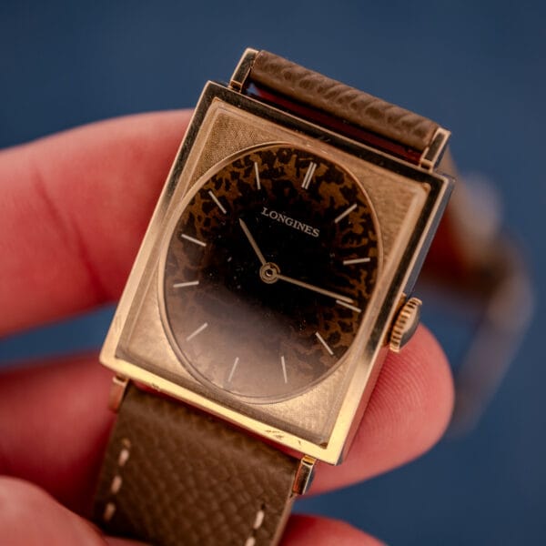 Tight in-hand macro of the Longines Tank 3217-428 Leopard dial showing the full tan, copper, and dark brown tortoiseshell patina pattern