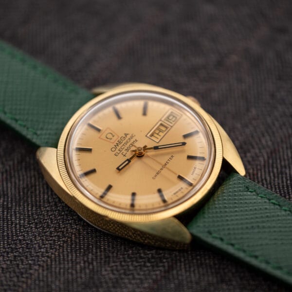 Three-quarter view of the Omega F-300 Hz showing the finely fluted gold-plated bezel and applied gold markers across the champagne dial