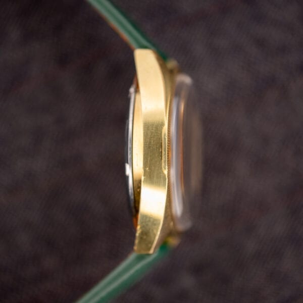 Left-side profile of the Omega F-300 Hz gold-plated case with the fluted bezel edge in shallow focus