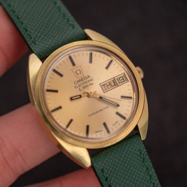 Omega Electronic F-300 Hz held in hand showing the fluted bezel and champagne day-date dial