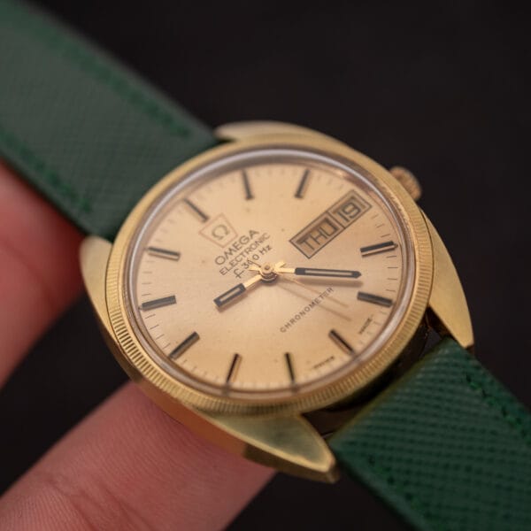 Omega F-300 Hz ref. 1980045 in hand against a dark background, fluted gold-plated bezel catching the light