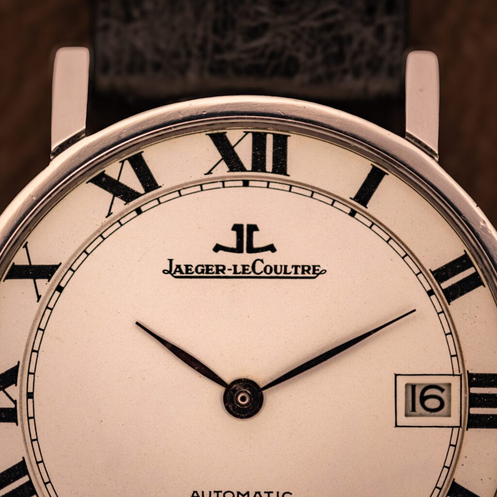 Jaeger LeCoultre Ultra Thin upper-dial macro showing applied JL monogram, cursive Jaeger-leCoultre signature, and inner railroad minute track.