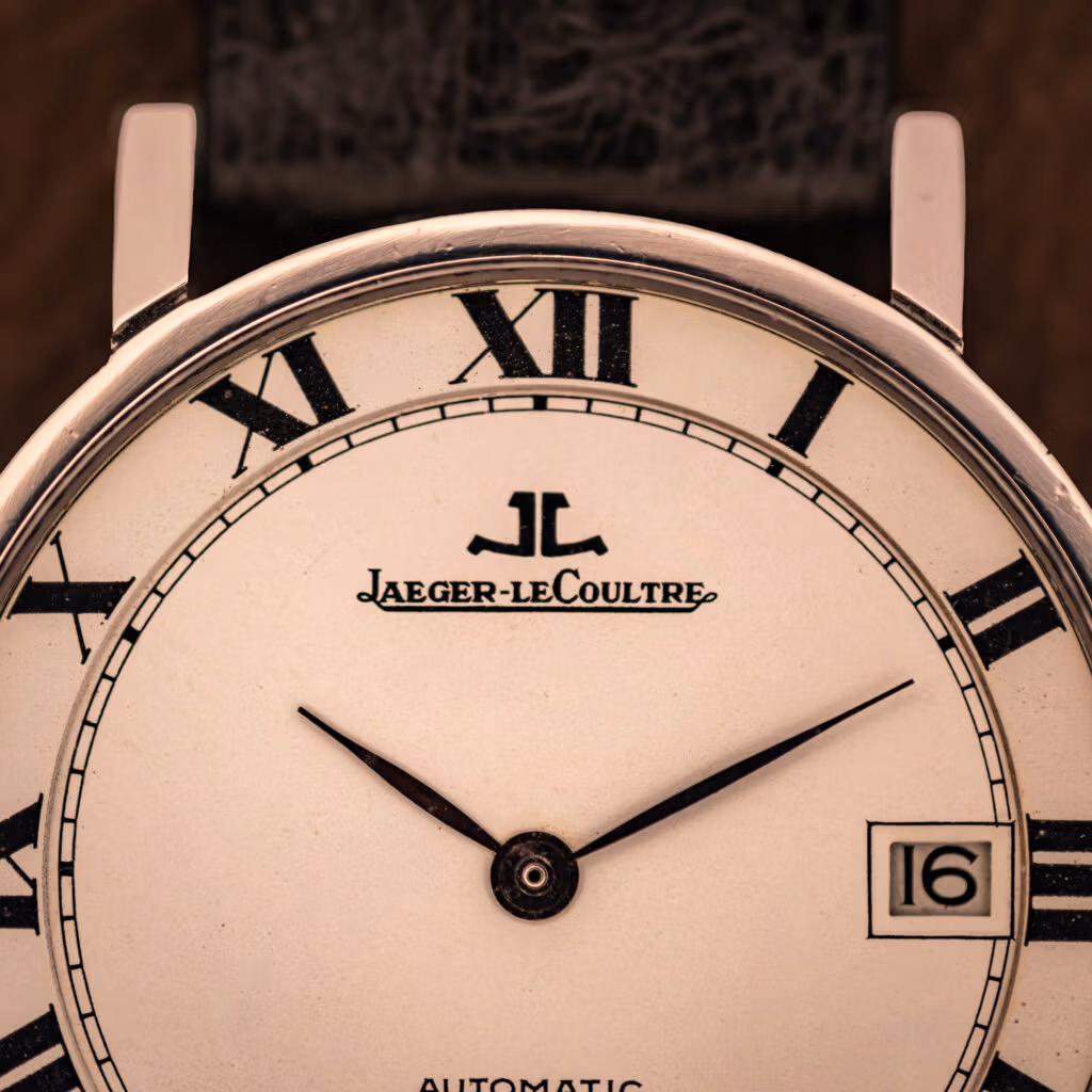 Jaeger LeCoultre Ultra Thin upper-dial macro showing applied JL monogram, cursive Jaeger-leCoultre signature, and inner railroad minute track.