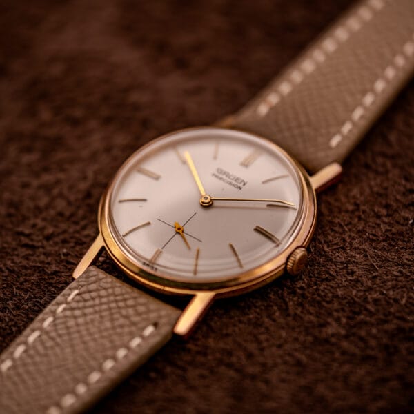 Gruen Precision 510 tilt view showing sunburst cream dial, gold-plated case, and contrast-stitched saffiano strap