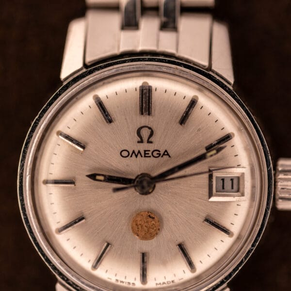 Omega Ladymatic 566.002 dial close-up showing baton hour markers, Omega logo, date window, and gold USS shield medallion