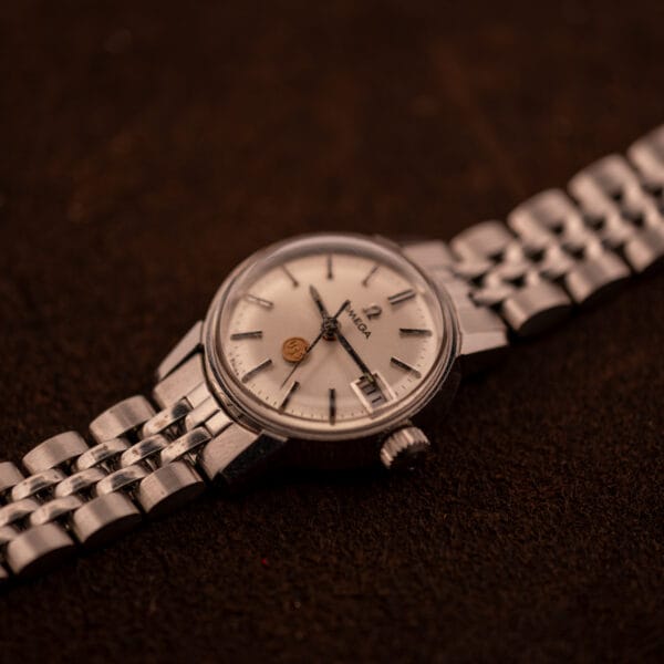 Three-quarter view of Vintage Omega Ladymatic 566.002 in hand showing dial, signed crown, and steel bracelet