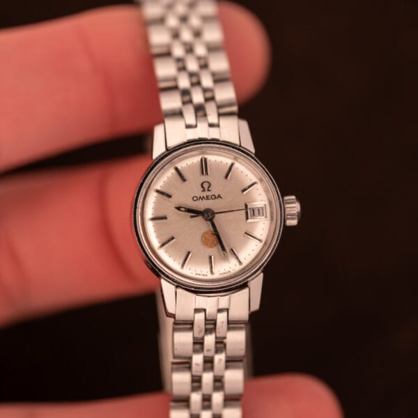 Wrist-shot of Omega Ladymatic 566.002 highlighting silver sunburst dial, date at 3, and USS gold medallion at 6