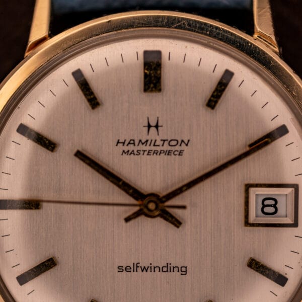 Hamilton Masterpiece dial close-up showing applied yellow gold dagger indices, Hamilton H-star logo, and selfwinding signature above six