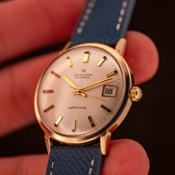 Hamilton Masterpiece selfwinding automatic in hand close-up with date window framed by the polished gold filled case