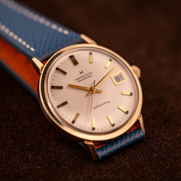 Hamilton Masterpiece Cal. 836 in hand showing silver sunburst dial, date complication, and SWISS signature at six