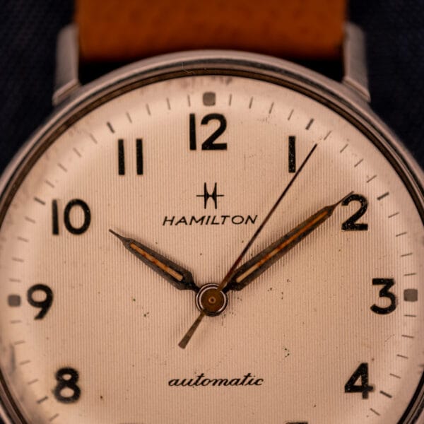 Hamilton Accumatic A-507 upper dial macro showing H logo, HAMILTON signature, and aged tritium-cream lume plots
