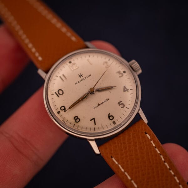 Hamilton Accumatic A-507 in-hand wrist context shot showing 33mm case proportions on tan leather