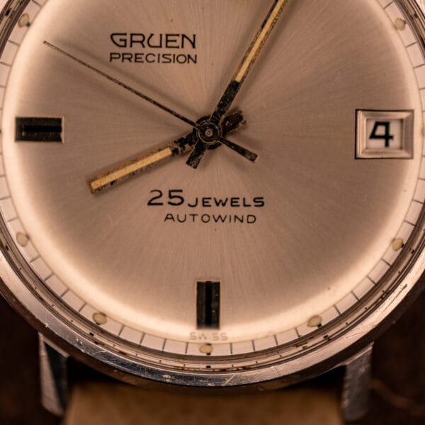 Gruen Precision silver sunburst dial macro with 25 JEWELS AUTOWIND text, date at three, and SWISS at six