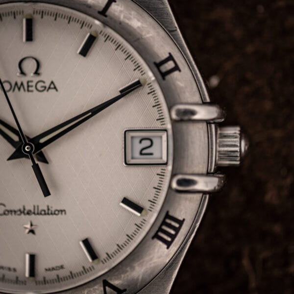 Omega Constellation 1512.30 macro of the date window at three, Omega-signed crown, and engraved Roman numerals II and III on the bezel