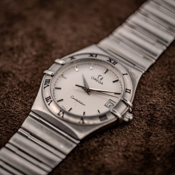 Omega Constellation Manhattan 1512.30 three-quarter angle on brown suede showing integrated 1552/862 bracelet and griffe case claws