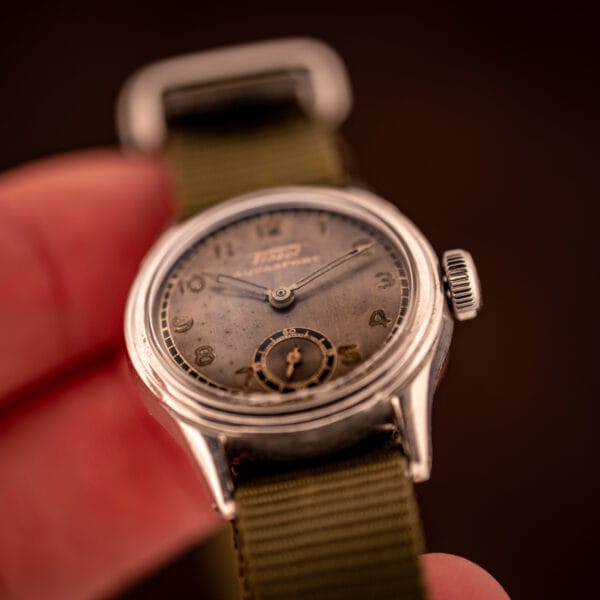 Tissot Aquasport on olive canvas military strap held in hand showing tropical patina dial and slim wartime case profile