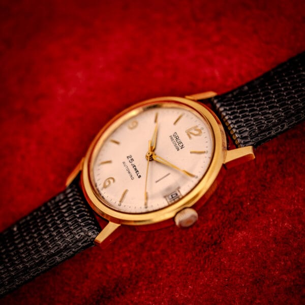 Vintage Gruen Precision angled wrist-ready shot, gold-tone bezel, silver sunburst dial, black lizard strap
