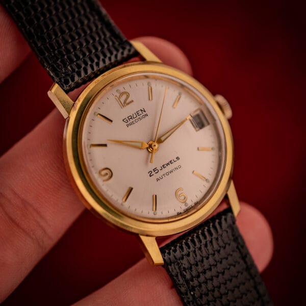 Vintage Gruen Precision hand-held shot showing gold-tone case scale, applied Arabic 12, date window, dauphine handset