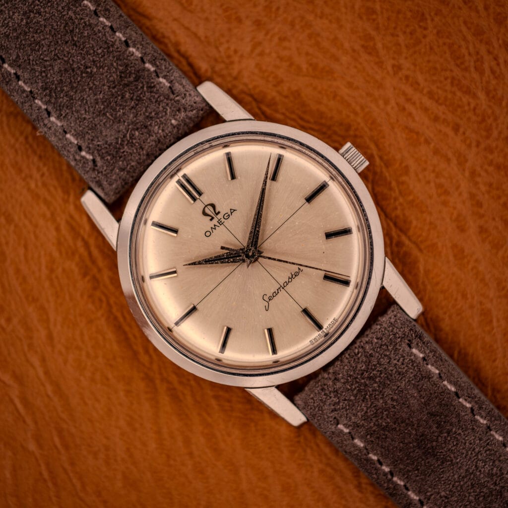 Omega Seamaster 135.005 with factory cross-hair silver sunburst dial on gray Italian suede strap, top-down view on amber leather