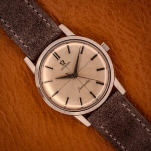 Omega Seamaster 135.005 with factory cross-hair silver sunburst dial on gray Italian suede strap, top-down view on amber leather