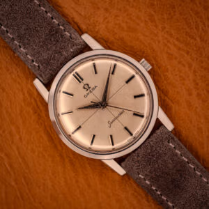 Omega Seamaster 135.005 with factory cross-hair silver sunburst dial on gray Italian suede strap, top-down view on amber leather