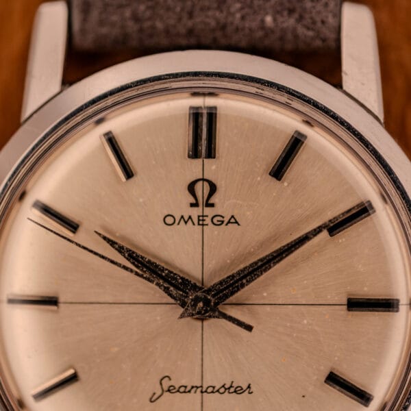 Omega Seamaster 135.005 dial macro showing applied Omega logo, baton hour markers, and aged dauphine hands on silver sunburst