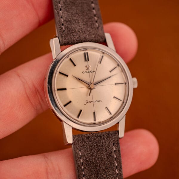 Vintage Omega Seamaster Ref. 135.005 wrist shot held in hand, gray suede strap visible against amber leather