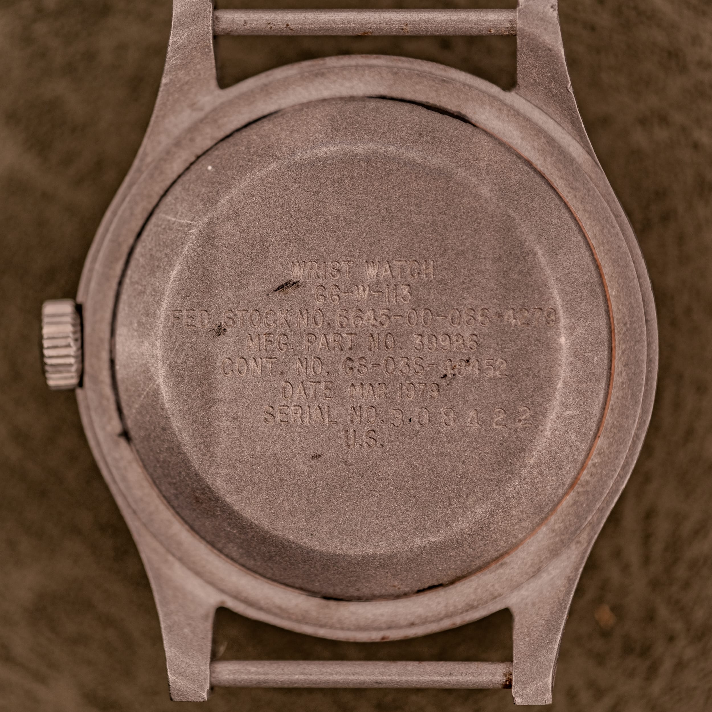 Back of a worn military wristwatch showing engraved specifications, serial number, and manufacturing details. Classic traits shared by vintage military watches like the IWC Mark XI or Dirty Dozen watches.