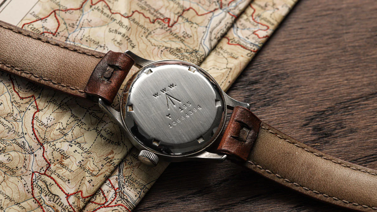 A vintage military watch with a brown leather strap rests on an old map, its engraved metal case back visible—a nod to classics like the IWC Mark XI and GG-W-113.