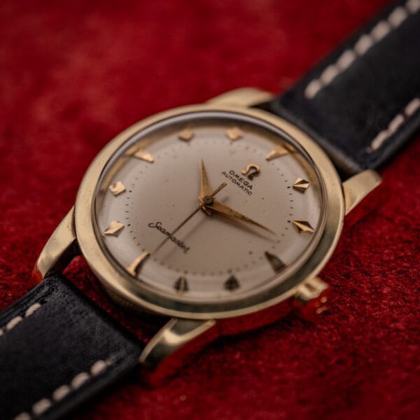 Omega Seamaster bumper automatic gold-capped dress watch with cream dial and black leather strap on red ground