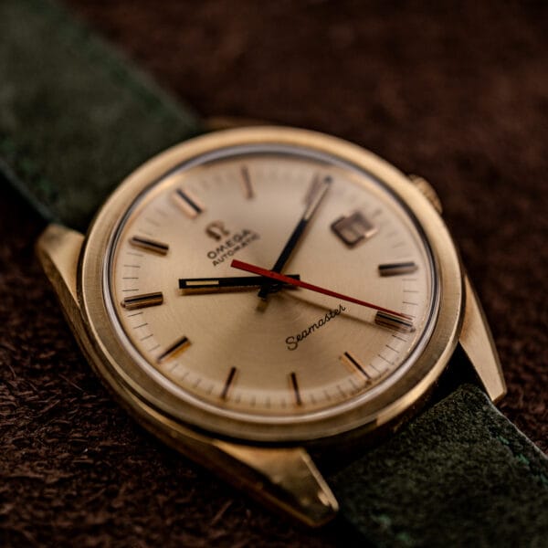 Vintage Omega Seamaster 166.028 gold cap with black baton hands and orange center seconds on green suede