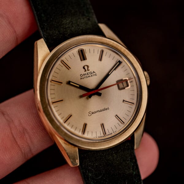 Omega Seamaster 166.028 gold-capped automatic held in hand, champagne dial with date at three and orange seconds