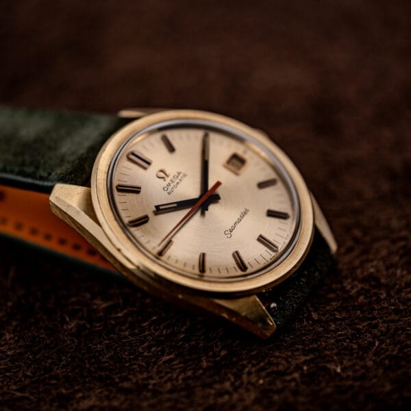 Omega Seamaster 166.028 resting on green Italian suede strap showing gold-capped case and downturned lugs